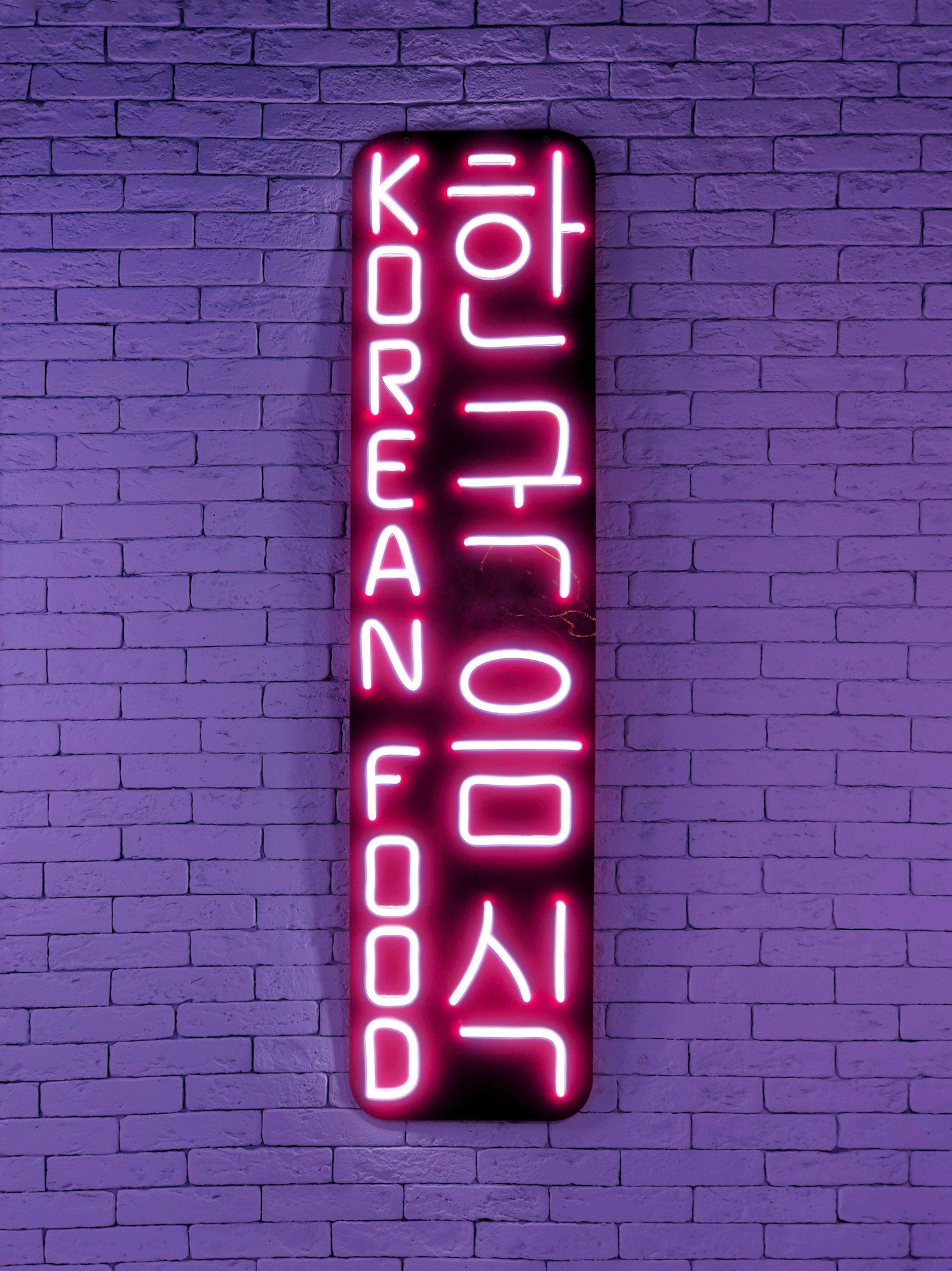 view of the neon composition of the word and hieroglyphs korean food on a purple brick wall